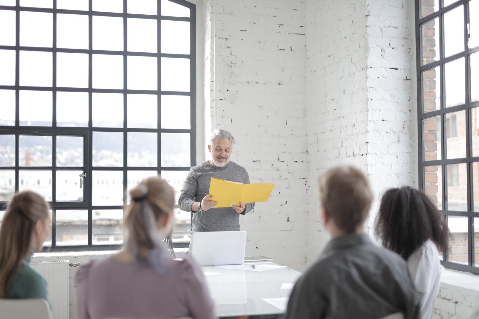 senior gray haired bearded male coach presenting ideas at diverse group meeting in modern office