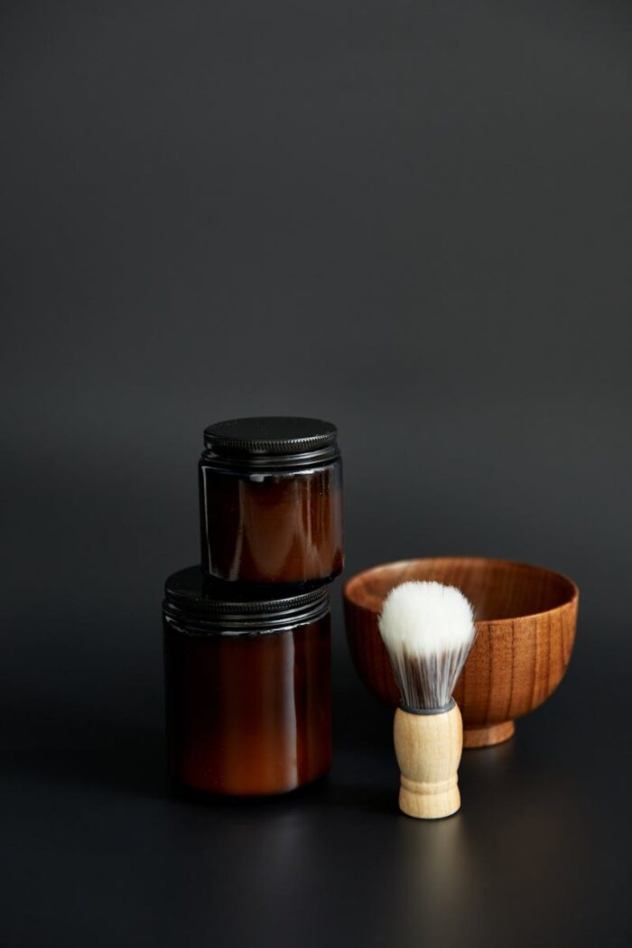Minimalist composition of a classic shaving set with containers and brush on a black background.